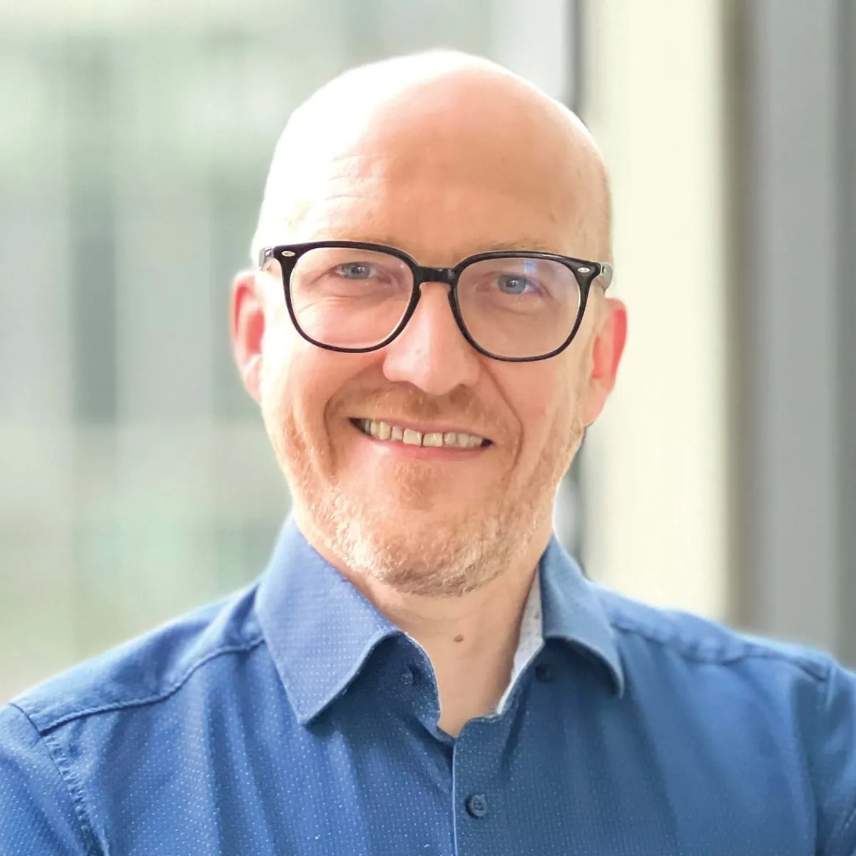 Ray, lächelnd, mit Brille und blauem Hemd